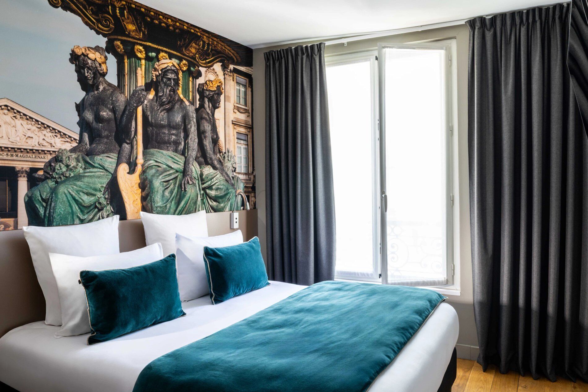 Una habitación de hotel con una cama grande, cortinas oscuras y un mural de estatuas clásicas.