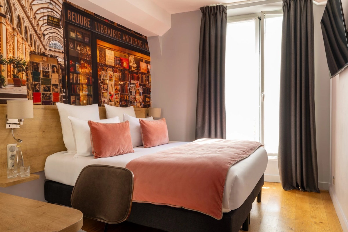 A hotel room with a bed, a desk, a chair, and a large window with curtains.