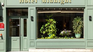 Un edificio con un letrero que dice "Hotel Midnight" y un amplio ventanal que muestra diversas plantas.