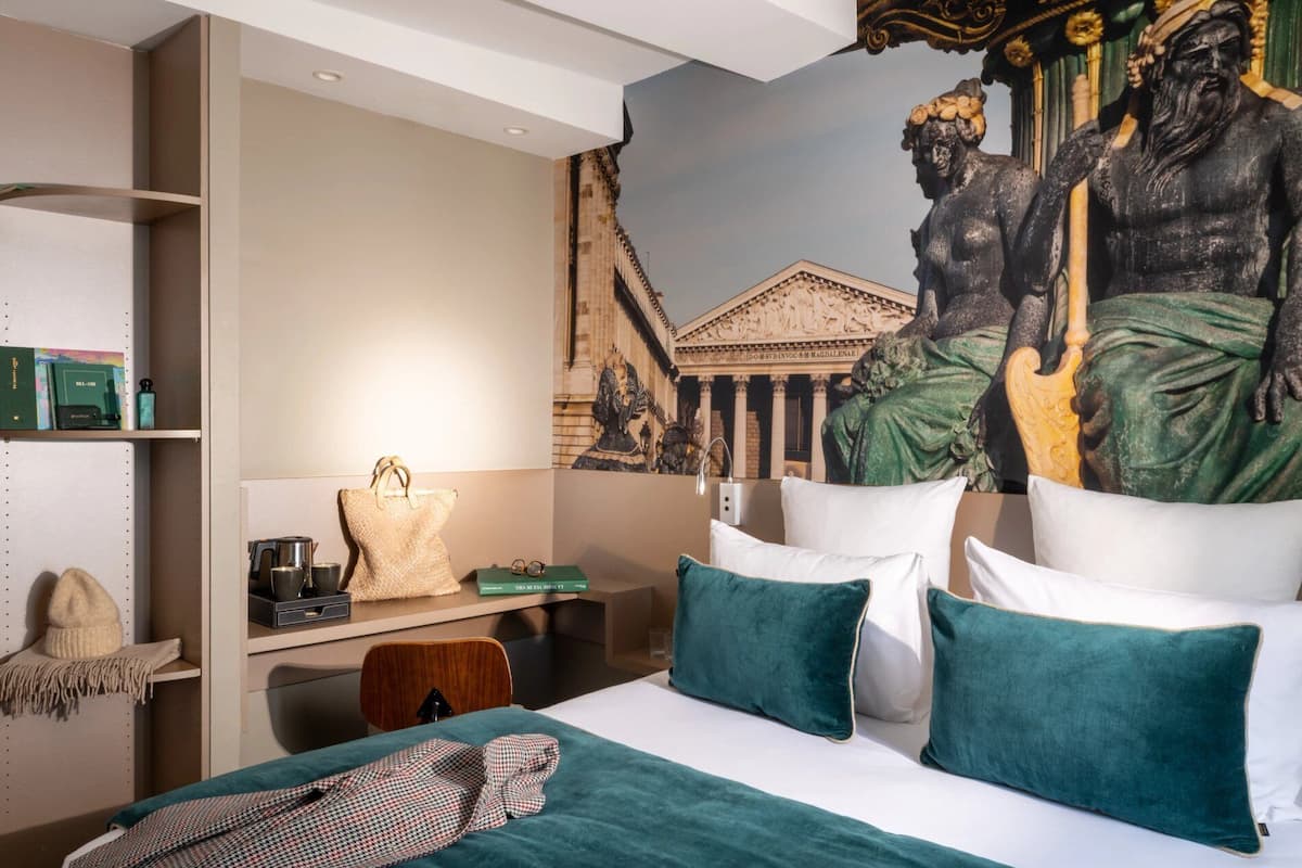 A hotel room with a bed, pillows, a desk, and a mural on the wall.