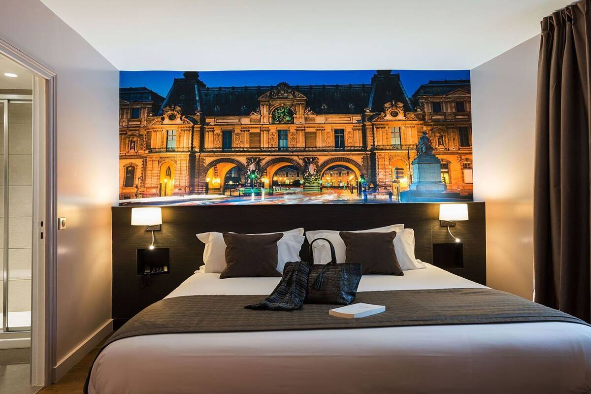 A hotel room with a large bed, two bedside tables, a nightstand, and a view of a historic building.