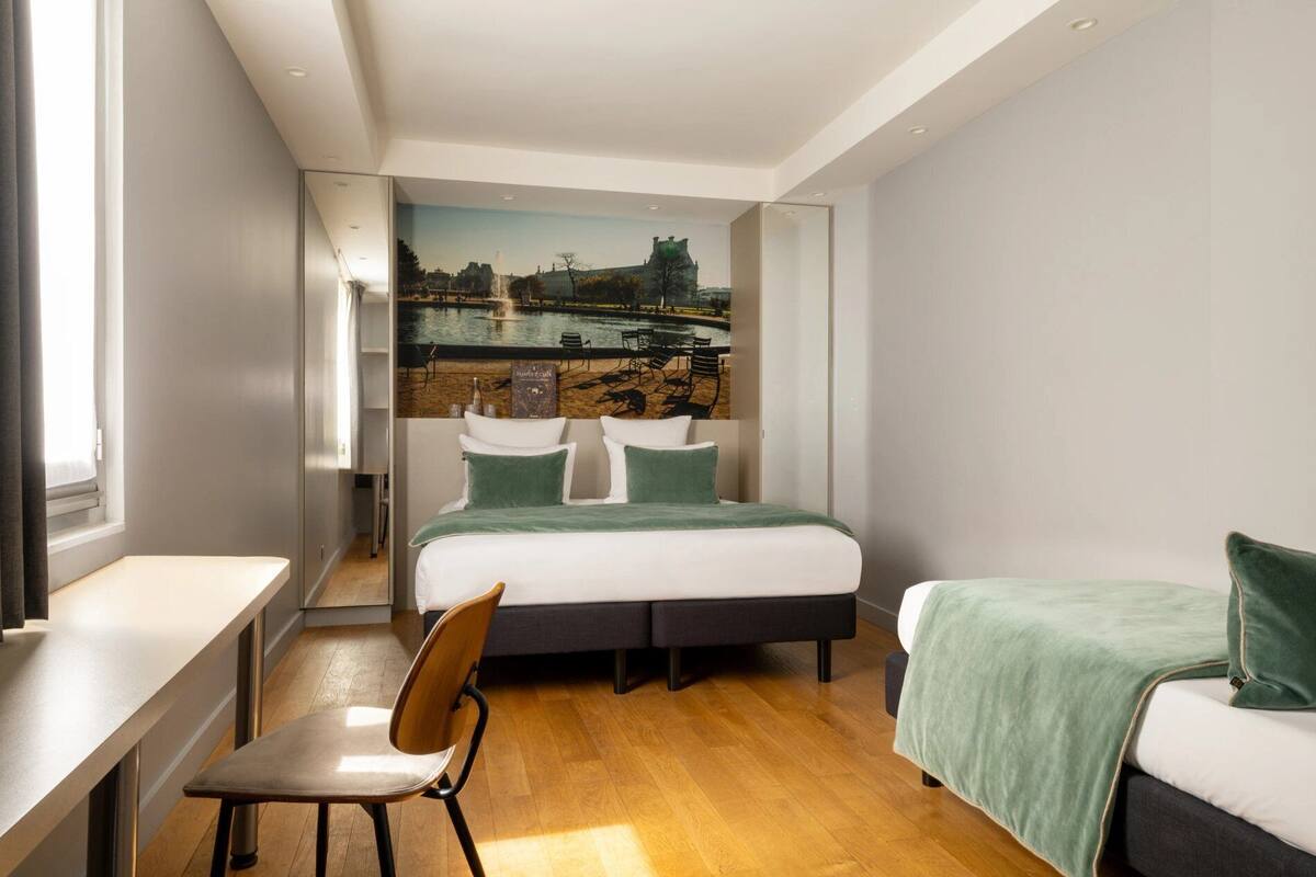 A modern bedroom with a bed, a chair, a desk, and a view of a park through a window.