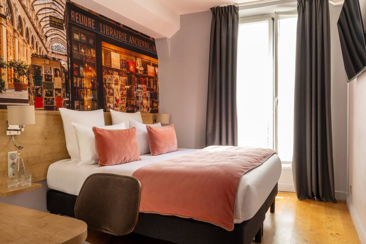 A hotel room with a bed, a desk, a chair, and a large window with curtains.