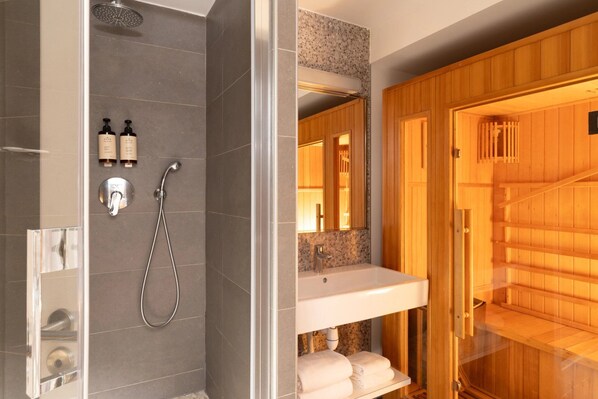 A modern bathroom with a shower, a vanity with a mirror, and a sauna area.