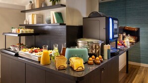 Un bufé de desayuno con diferentes alimentos, una máquina de café y una selección de libros en estanterías.