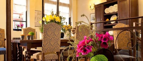 A traditional room with patterned furniture, a wooden cabinet with dishes, and various potted plants.