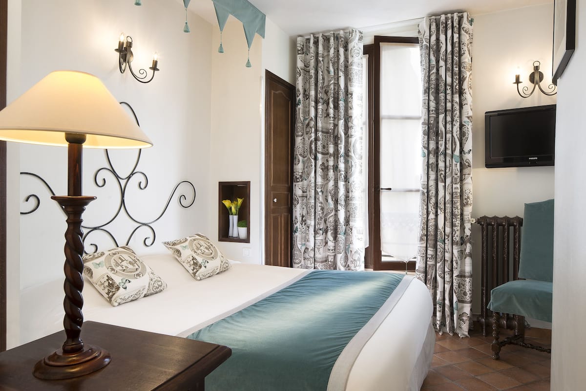 A hotel room with a bed, a lamp, a TV, and curtains.