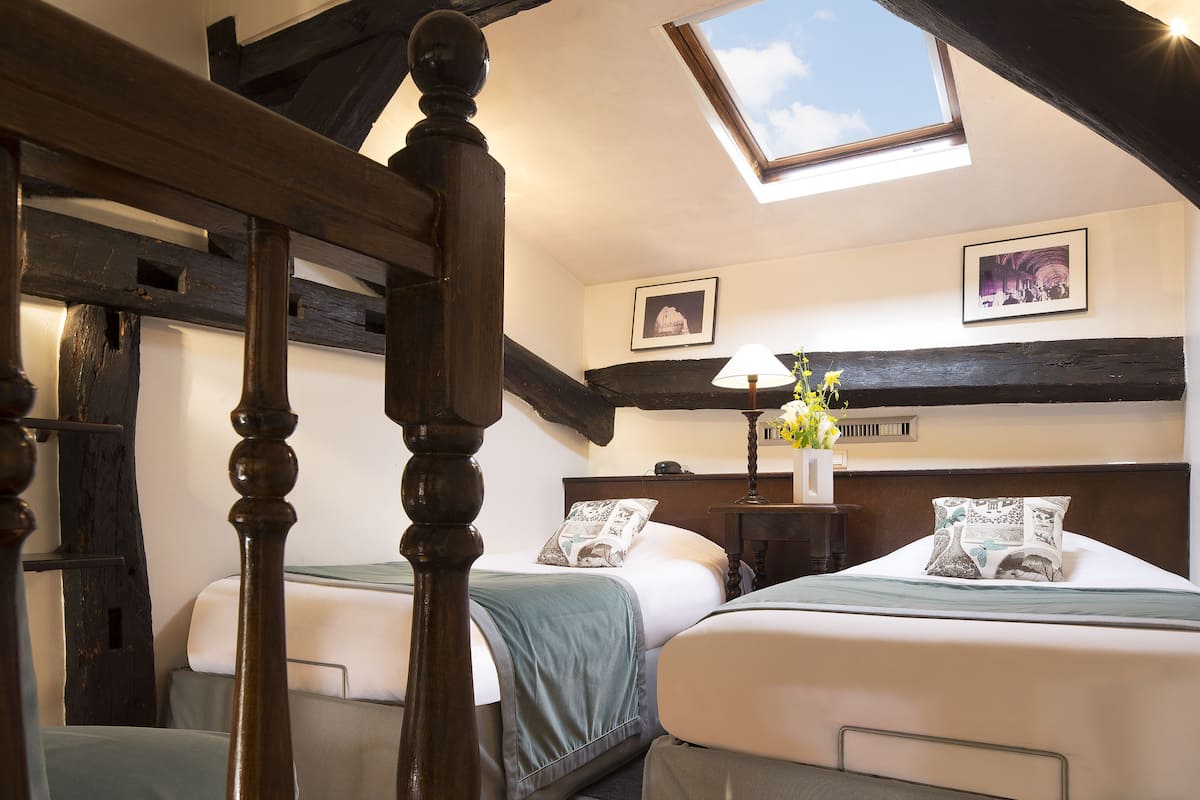 A bedroom with two beds, a skylight, and a nightstand with a lamp and flowers.