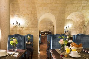 A dining area with stone walls, blue patterned booths, and breakfast items like croissants and orange juice.