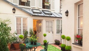 A courtyard with a round table and chairs, potted plants, and a door leading to a room.