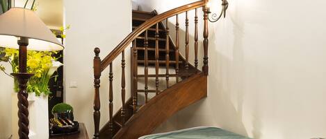 A bedroom with a wooden staircase, a bedside table with a lamp, and a bed with a green bedspread.