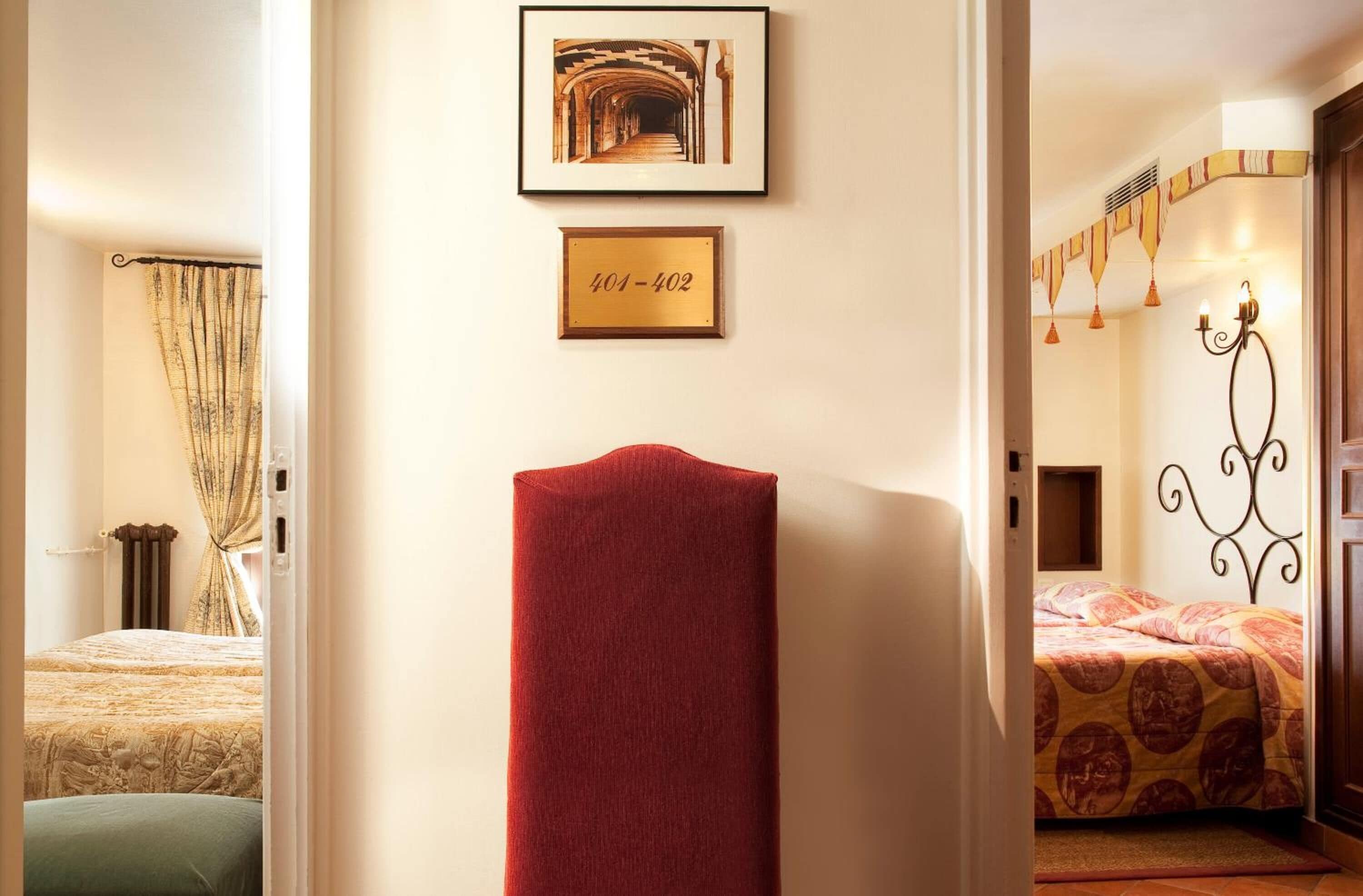 Een hotelkamer met een bed, een rode stoel, een lijst met een afbeelding en een deur naar een andere kamer.