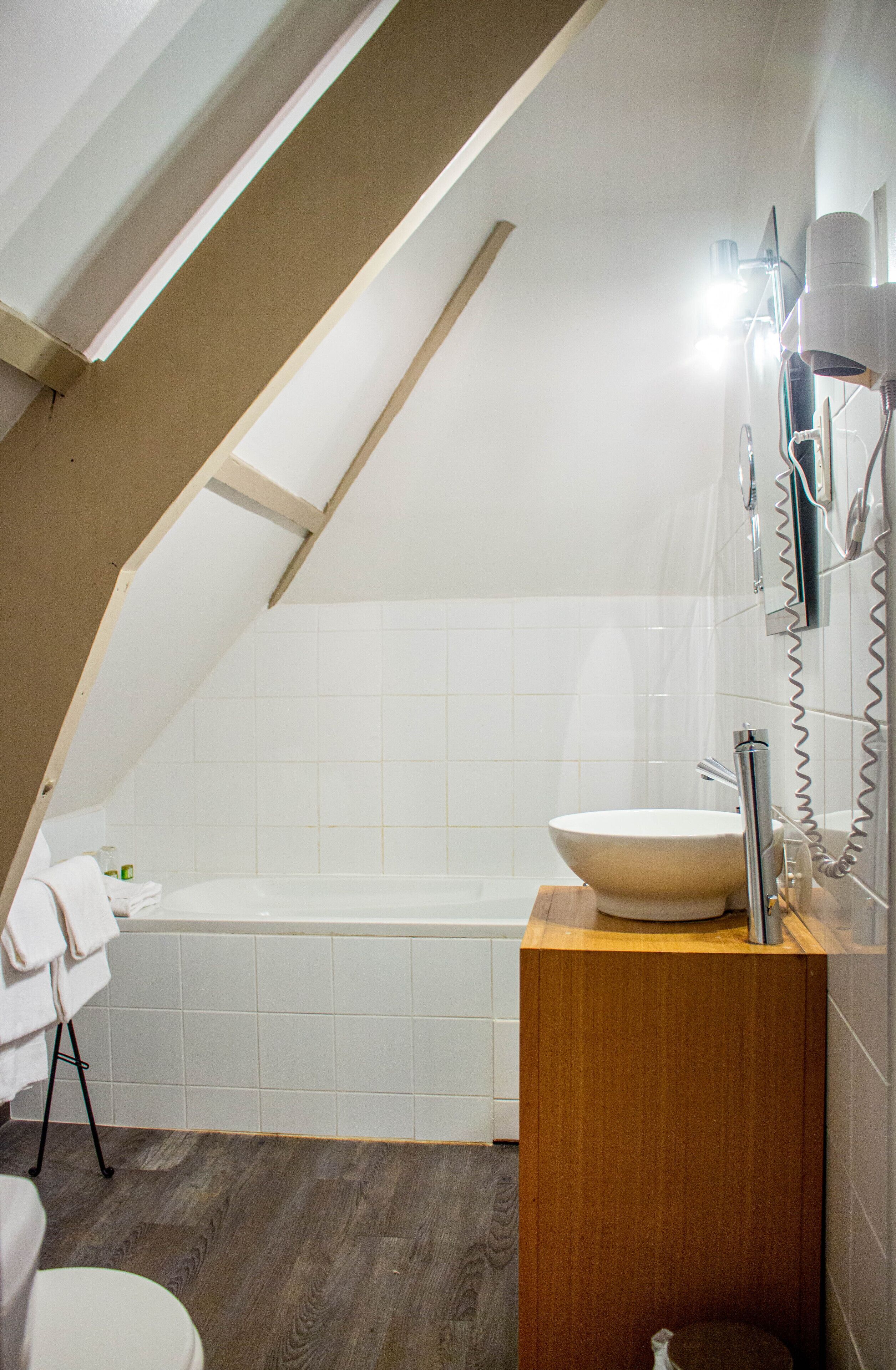 Une salle de bain avec un plafond en pente, une baignoire, un meuble-lavabo en bois et un lavabo blanc.