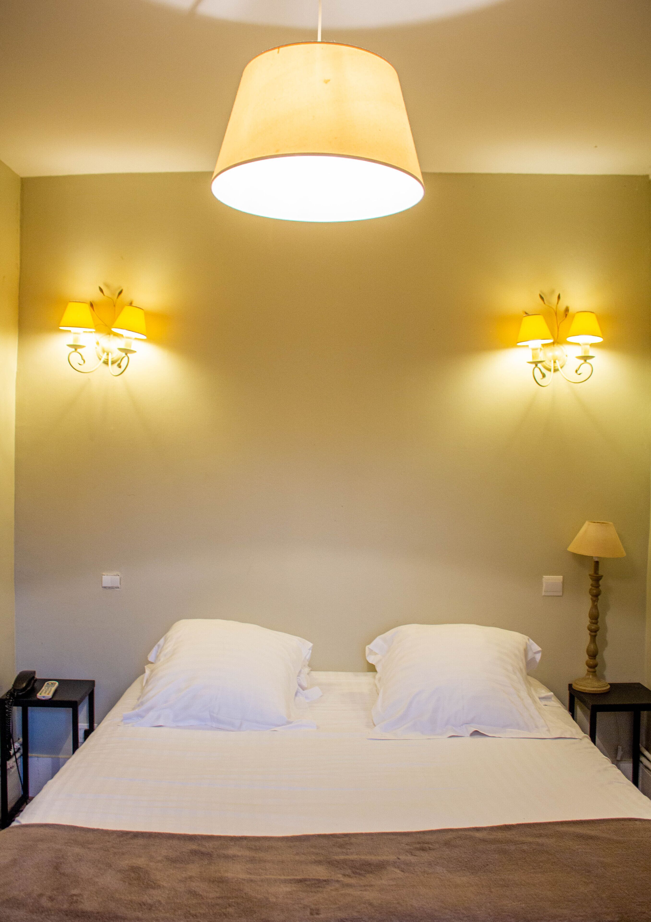 Una habitación de hotel con una cama, dos lámparas de noche y una lámpara colgante.