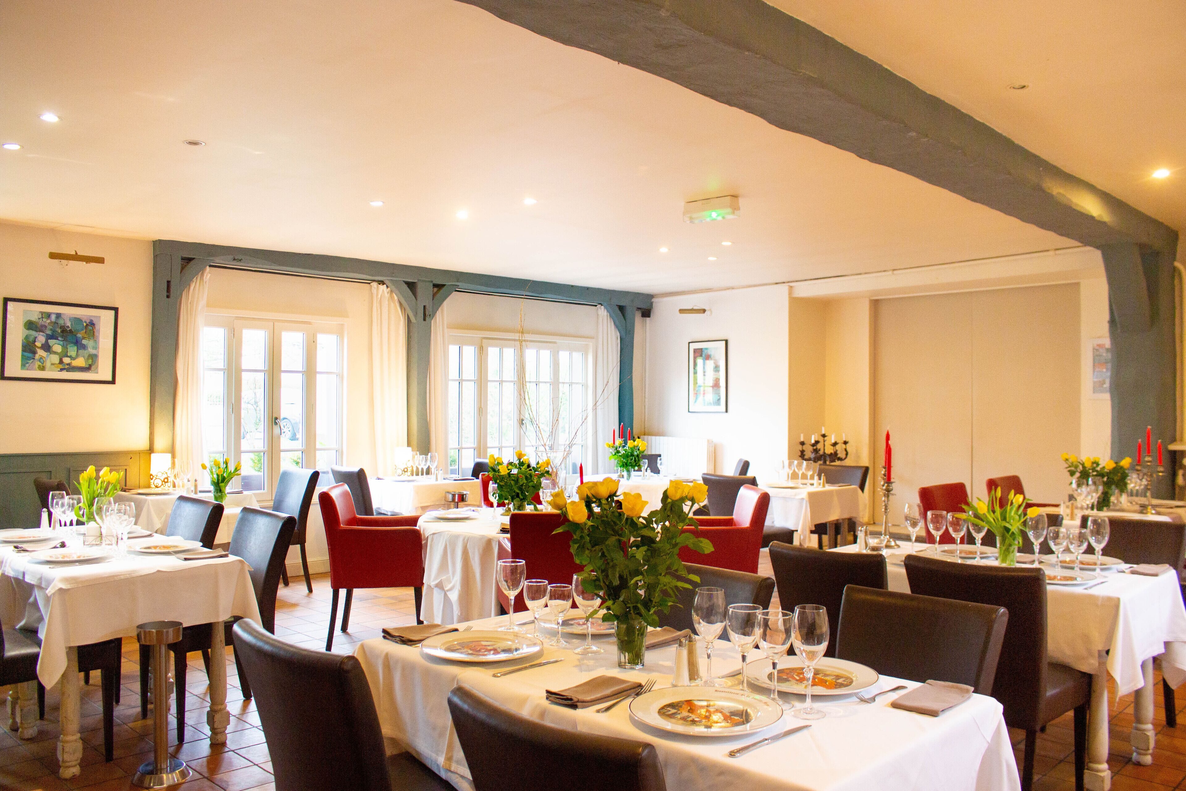A restaurant with multiple tables set for dining, featuring white tablecloths, chairs, and floral centerpieces.