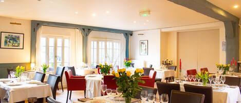A restaurant with multiple tables set for dining, featuring white tablecloths, chairs, and floral centerpieces.