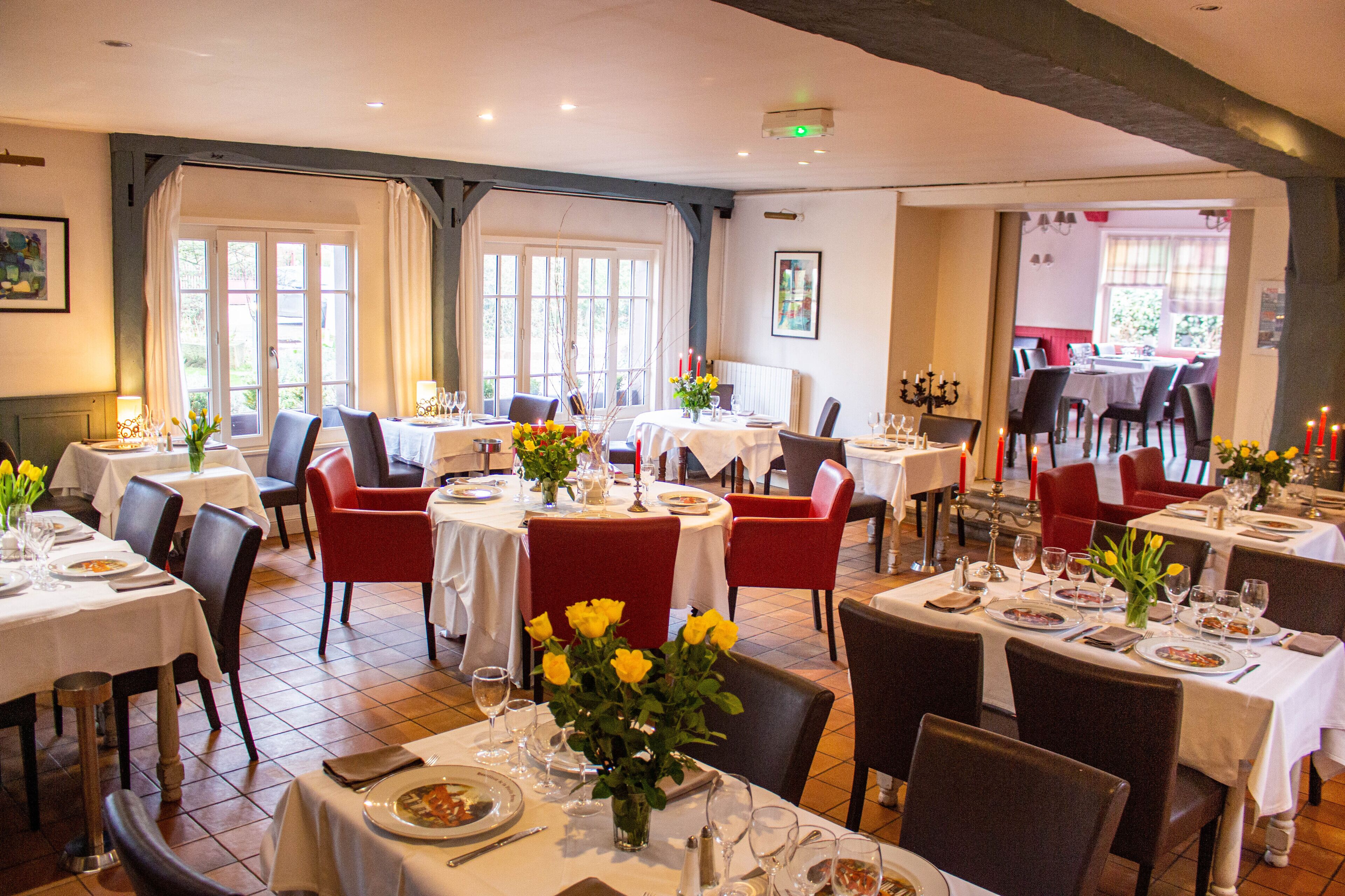 A restaurant with multiple tables and chairs, each set with plates, glasses, and flowers.