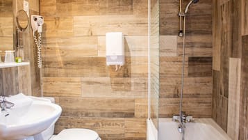 Een badkamer met een houten wand, een witte wastafel, een toilet en een douchecel met glazen wanden.