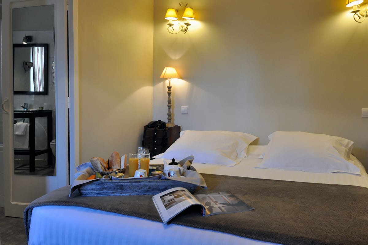 Une chambre d’hôtel avec un lit, une table de chevet avec une lampe, un miroir et un plateau de petit-déjeuner.