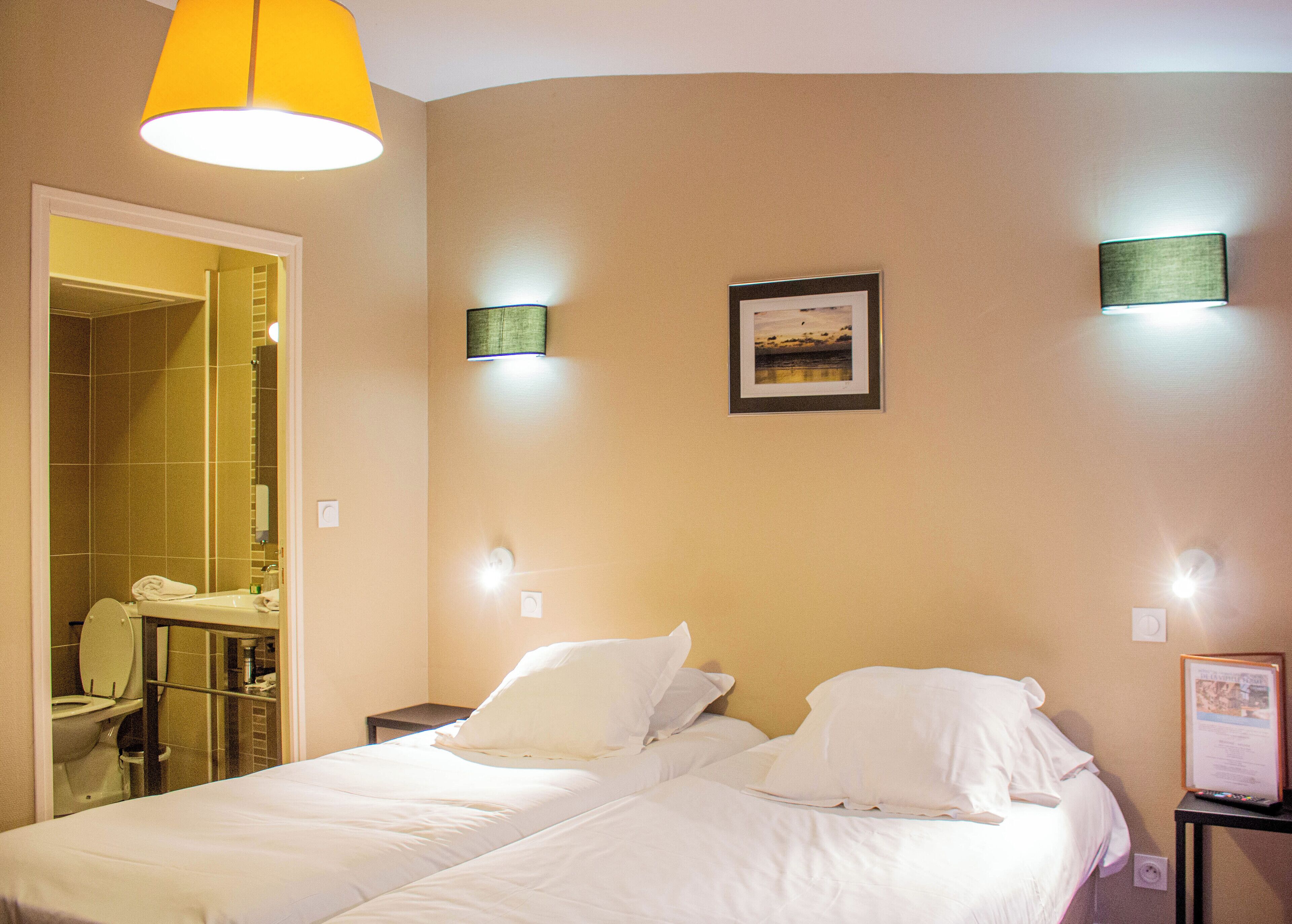 A hotel room with a bed, a nightstand, a framed picture on the wall, and a bathroom visible through an open door.