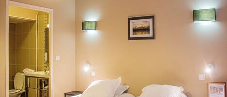 A hotel room with a bed, a nightstand, a framed picture on the wall, and a bathroom visible through an open door.