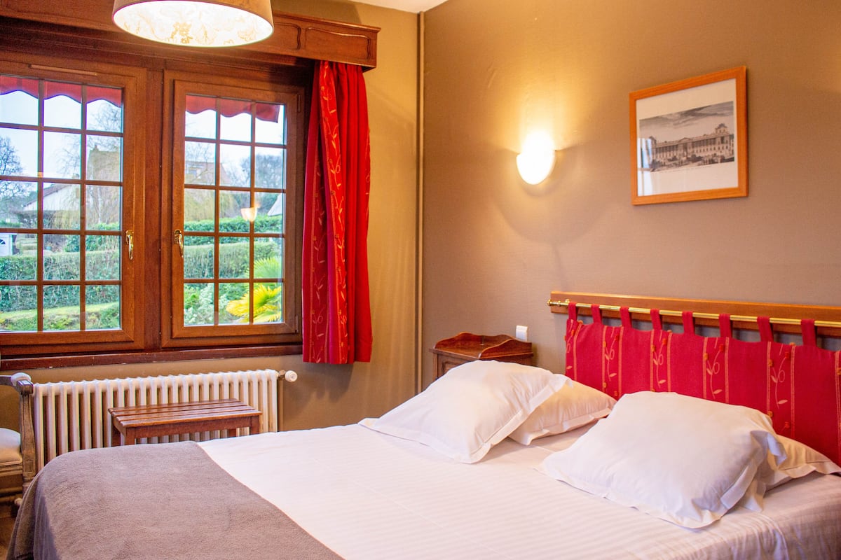 Une chambre à coucher avec un lit, une fenêtre avec des rideaux, un radiateur, une table de chevet et une lampe fixée au mur.