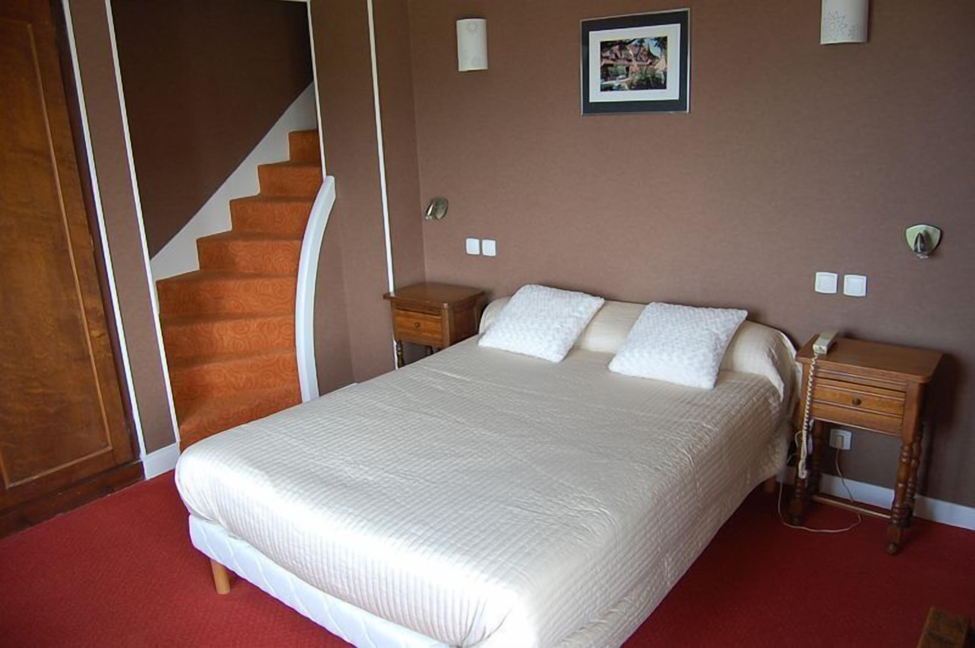 Ein Schlafzimmer mit einem großen Bett, einem hölzernen Nachttisch, einem kleinen Tisch, einem Bild an der Wand und einer Treppe.