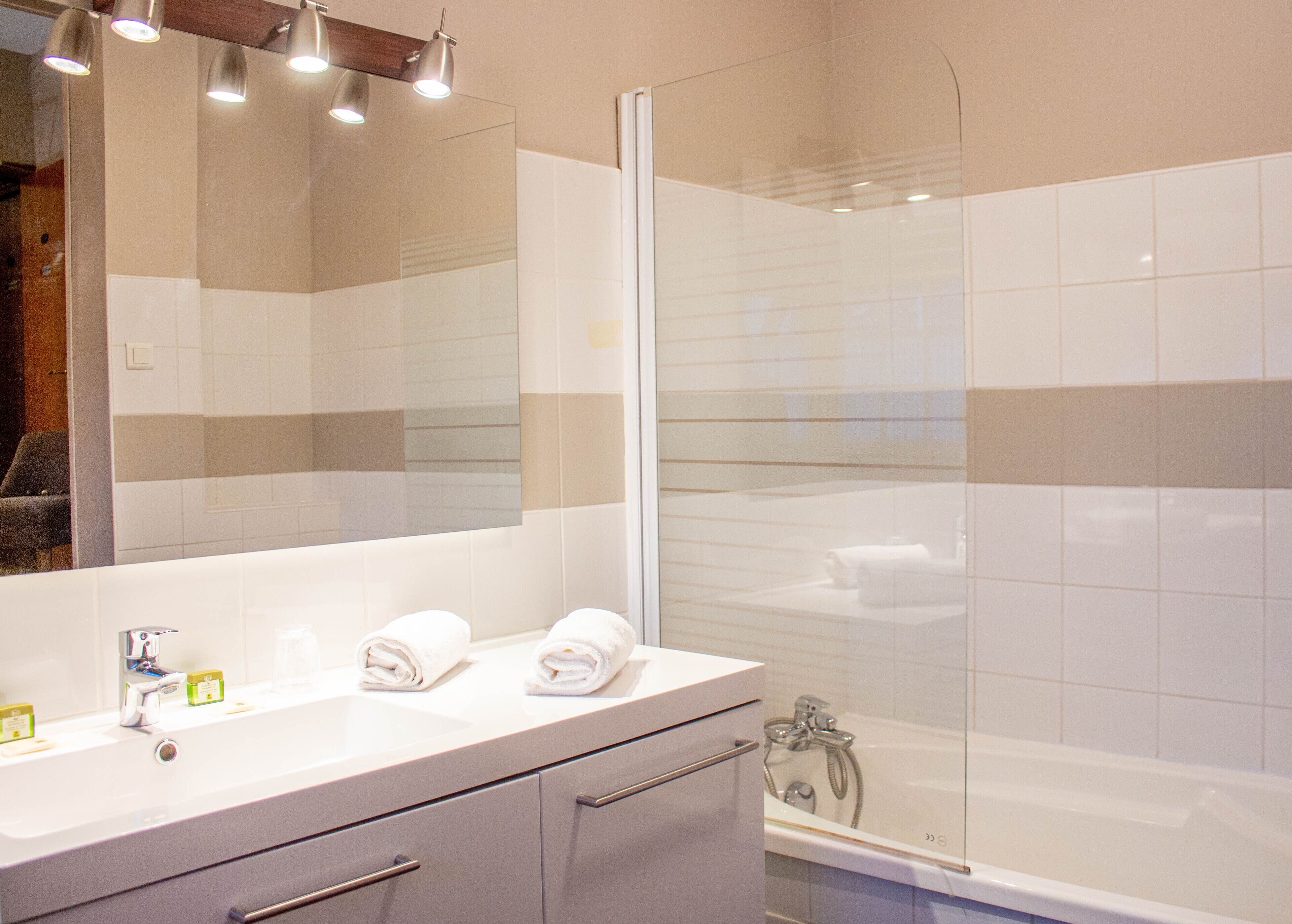 A modern bathroom with a large mirror, a white sink, two towels, and a glass shower enclosure.