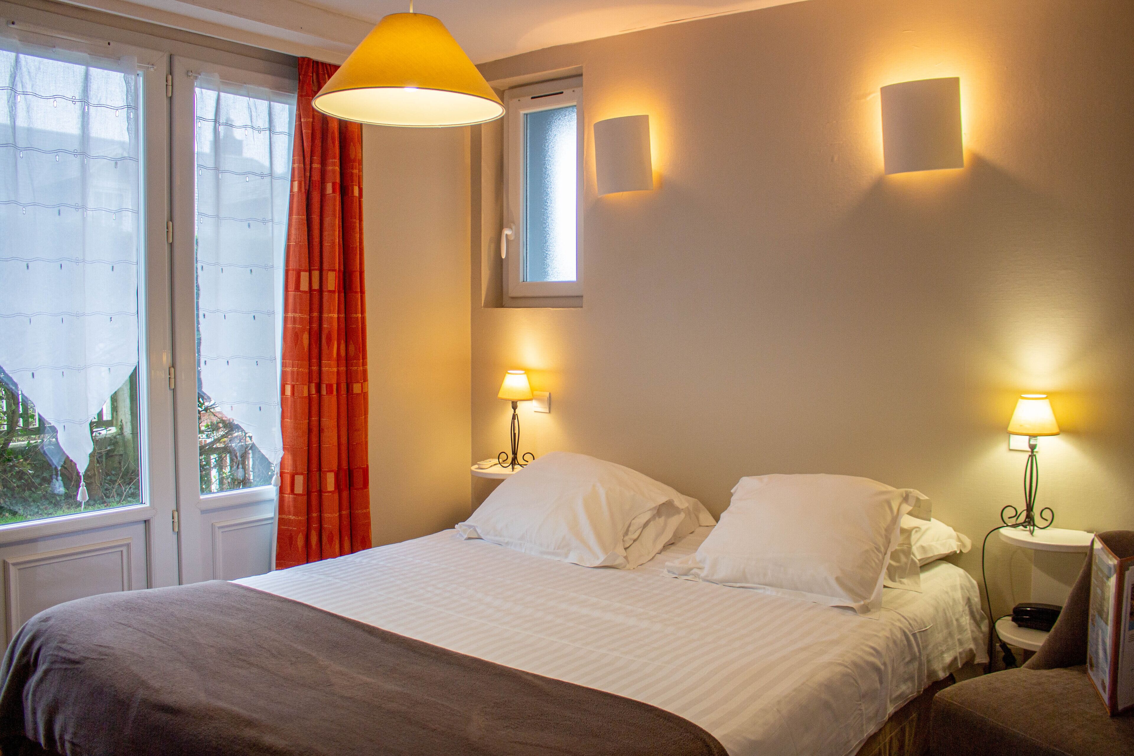 Een hotelkamer met een bed, twee nachtkastjes, een raam met gordijnen en wandlampen.