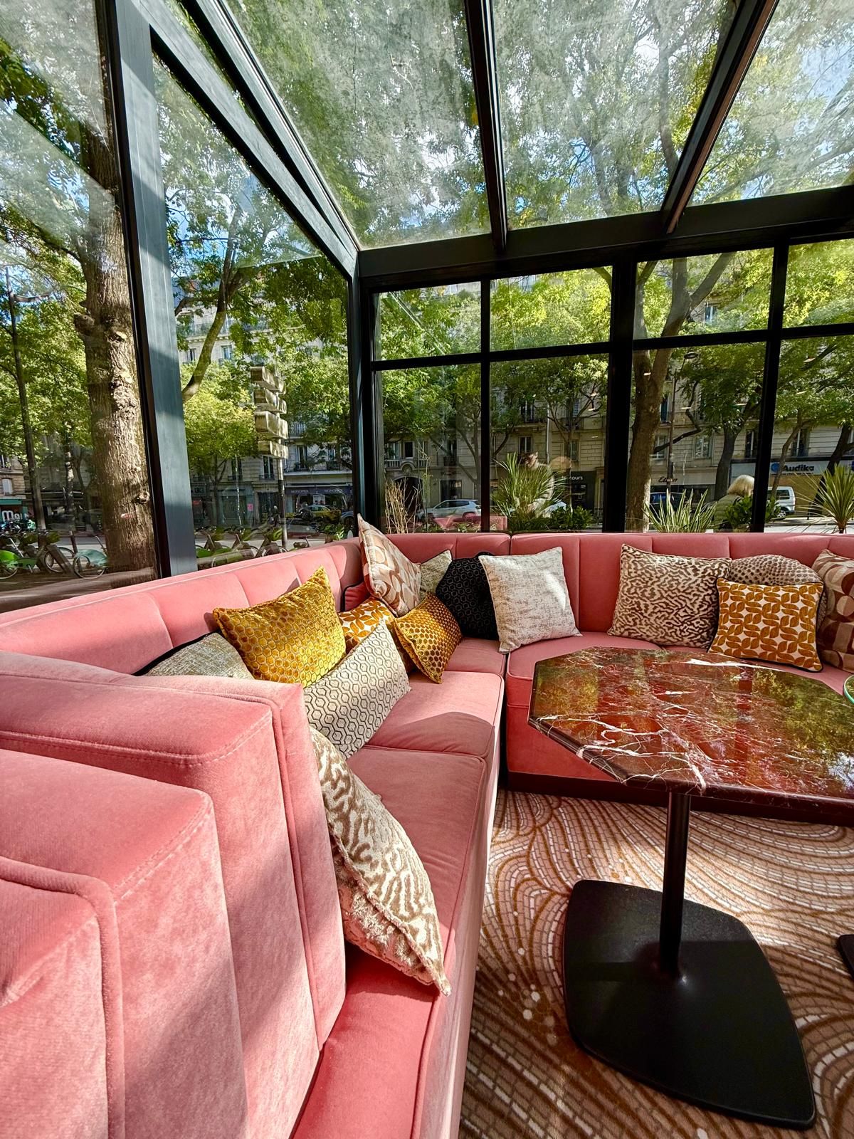 A modern living room with a pink sofa set, patterned cushions, and a glass coffee table.