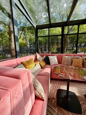 A modern living room with a pink sofa set, patterned cushions, and a glass coffee table.