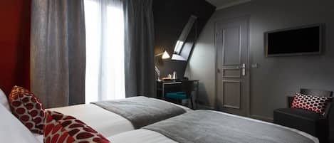 A hotel room with two beds, a desk, a chair, a TV, and a window with curtains.