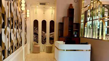 A hotel lobby with a reception desk, a patterned wall, and a mirror reflecting the interior.