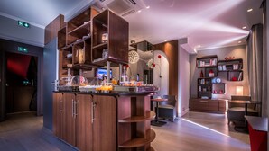 Een moderne hotellobby met een centraal houten bar, zitplaatsen en een boekenplank met boeken en decoratieve objecten.