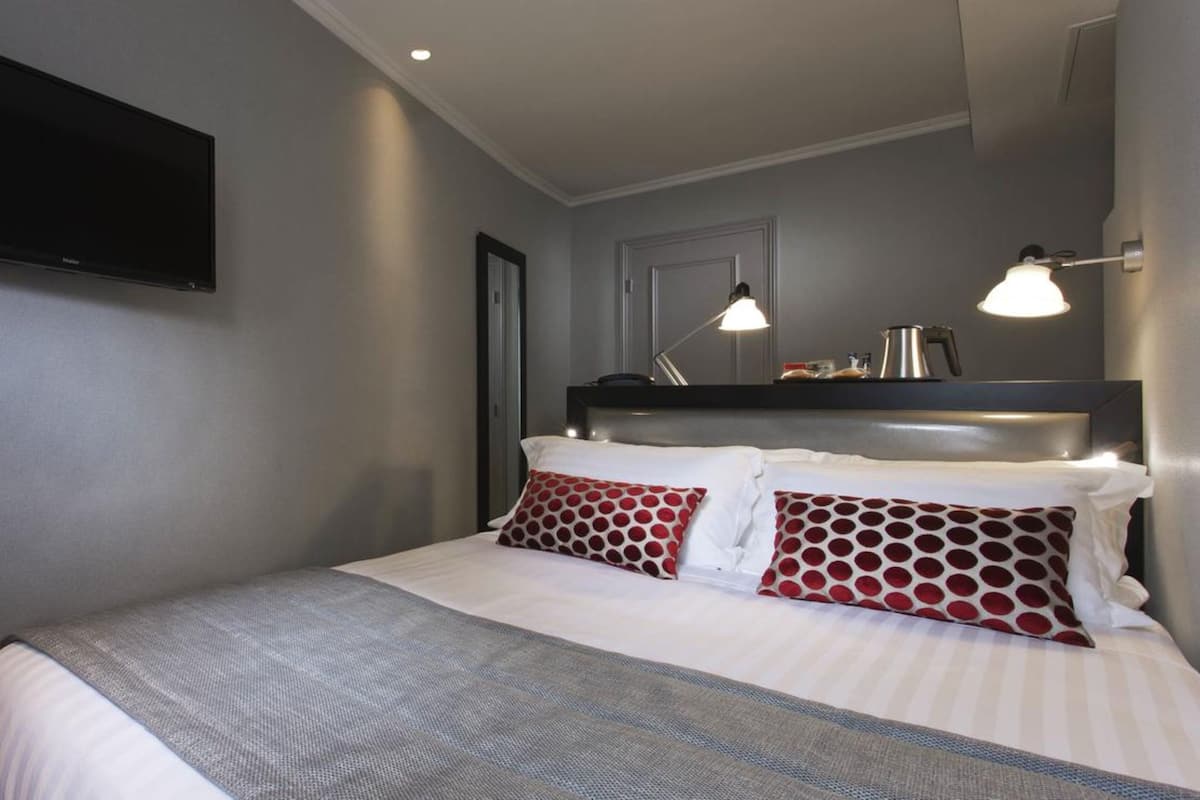Ein Hotelzimmer mit Bett, einem flachbildfernseher an der Wand und zwei Nachttischlampen.