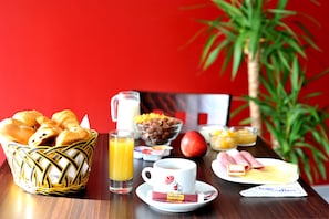 A breakfast table with croissants, orange juice, a coffee cup, a bowl of cereal, a ham sandwich, and a fruit bowl. - Hotel initial by balladins Roissy CDG / Saint-Mard (Saint-Mard)