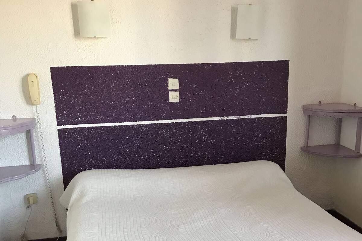 A room with a bed, a telephone, and a small shelf.