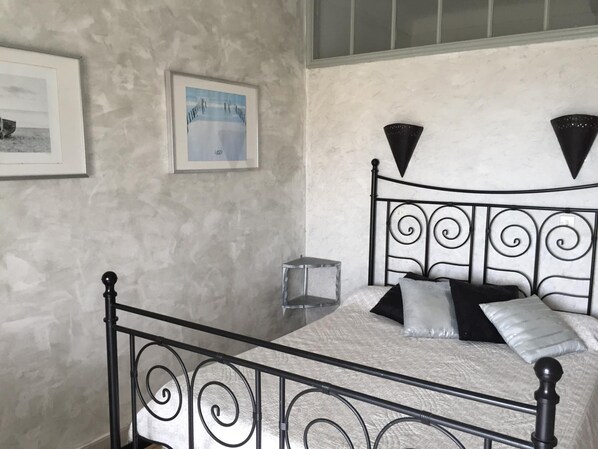 Un dormitorio con estructura metálica para la cama, una mesita de noche y una repisa en la pared.