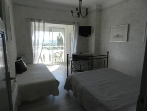 A bedroom with two beds, a TV, and a balcony with a chair. - Hôtel Paradis (Bormes-Les-Mimosas)