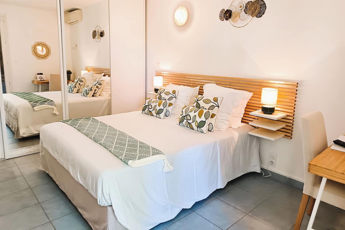 Una habitación de hotel con una cama grande, una mesita de noche con lámpara, un espejo y un adorno en la pared.