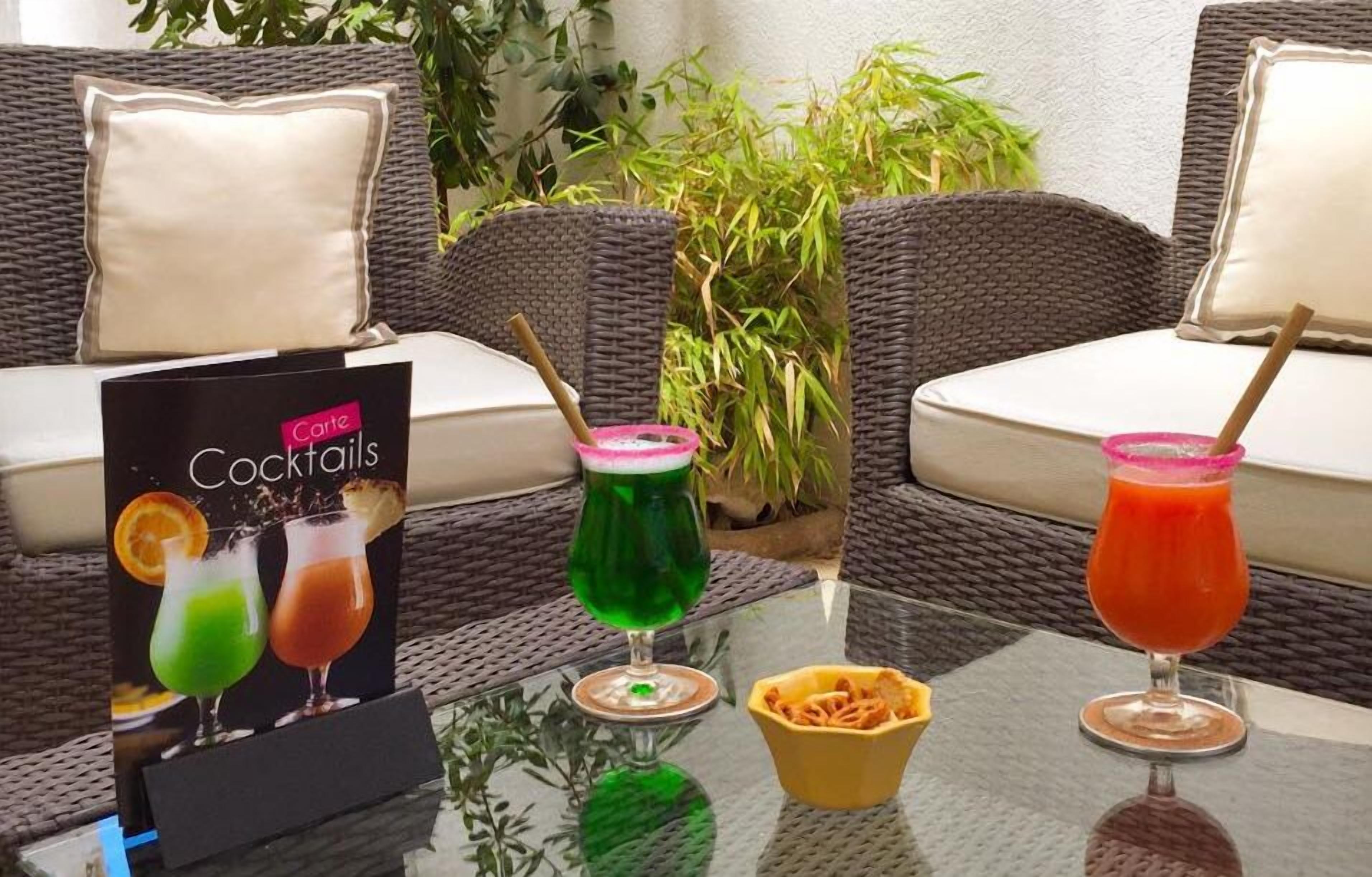 Menu de cocktails sobre uma mesa com duas cadeiras de vime e um almofado.