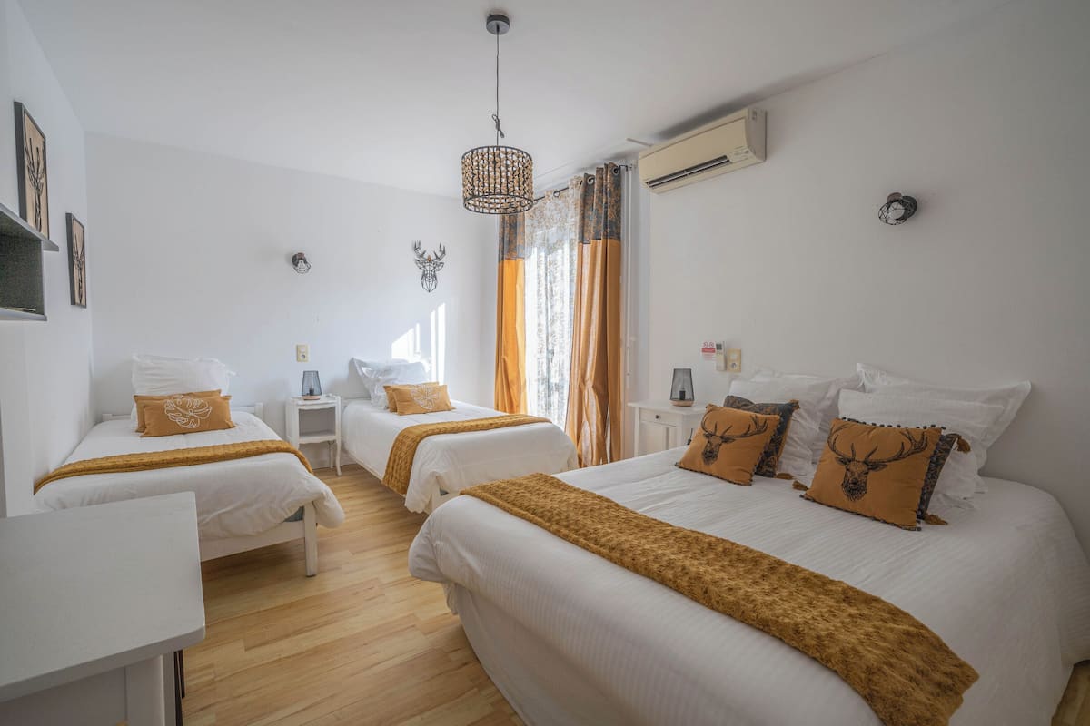 Una habitación de hotel con dos camas, un escritorio blanco, una mesita pequeña y un ventanal con cortinas.
