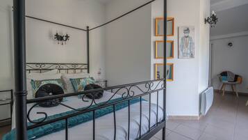 A four-poster bed with a teal throw blanket, a white mattress, and decorative pillows. There is a wall-mounted light fixture above the bed and a framed artwork on the wall.