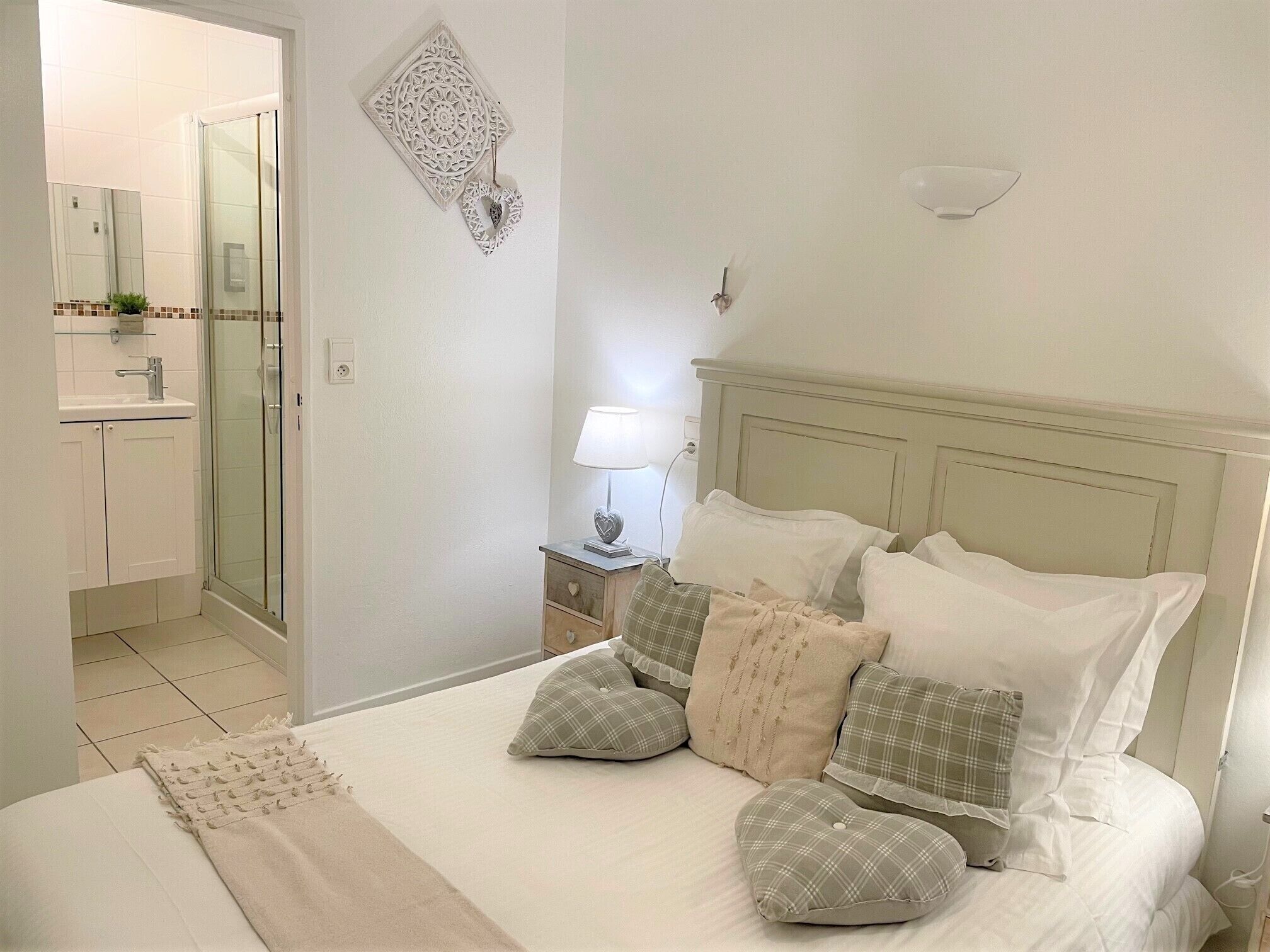 A bedroom with a bed, bedside table, lamp, and a bathroom with a mirror and sink.