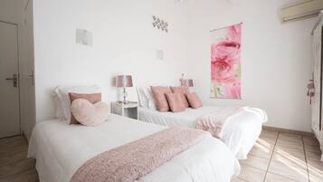 Quarto com duas camas, um lustre, ar-condicionado na parede e uma obra de arte floral.