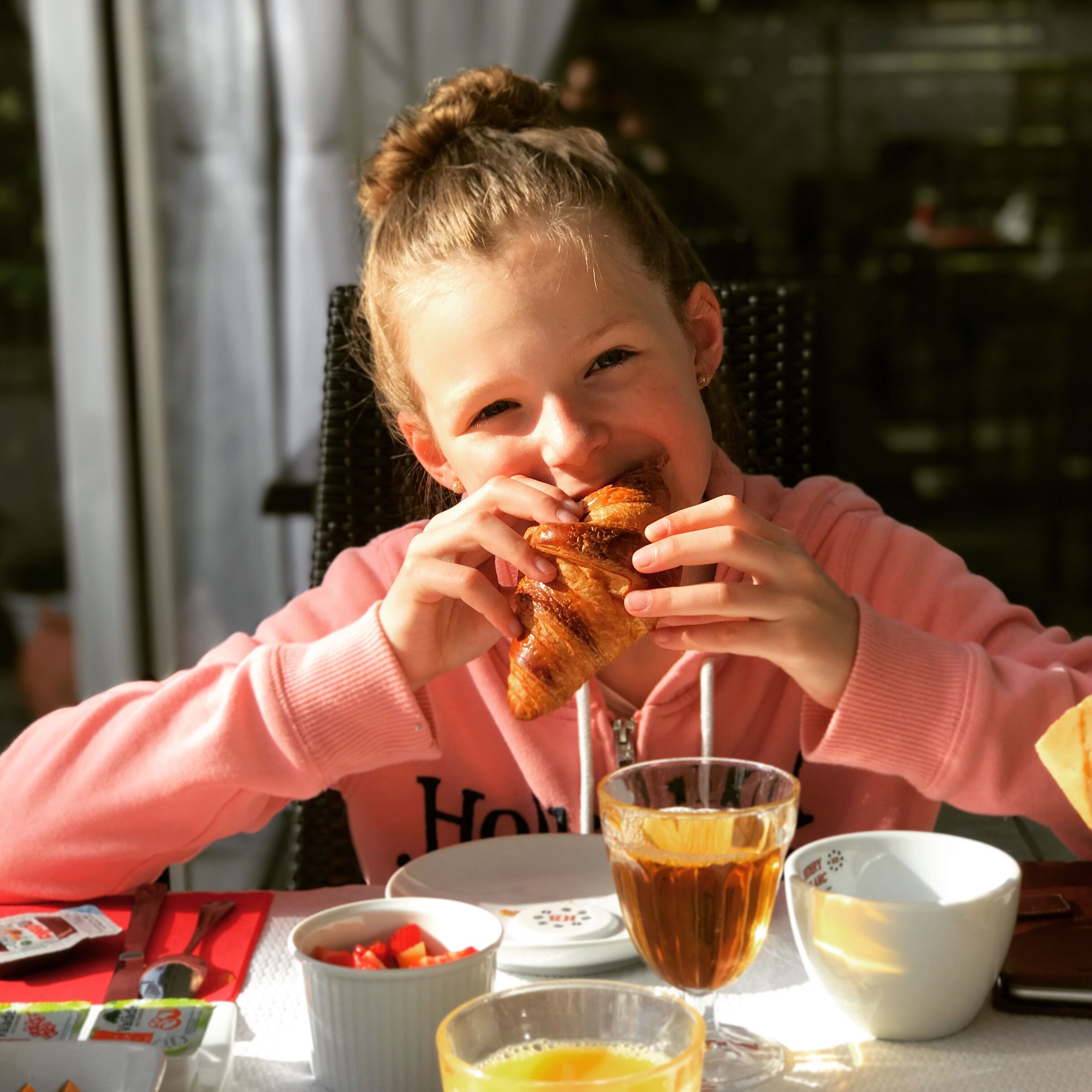 Una persona sentada a una mesa con un plato de comida, un vaso de líquido ámbar y un bol de alimento.