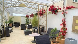 Un espace patio intérieur aménagé avec des meubles en osier, des plantes en pot et une structure métallique décorative.