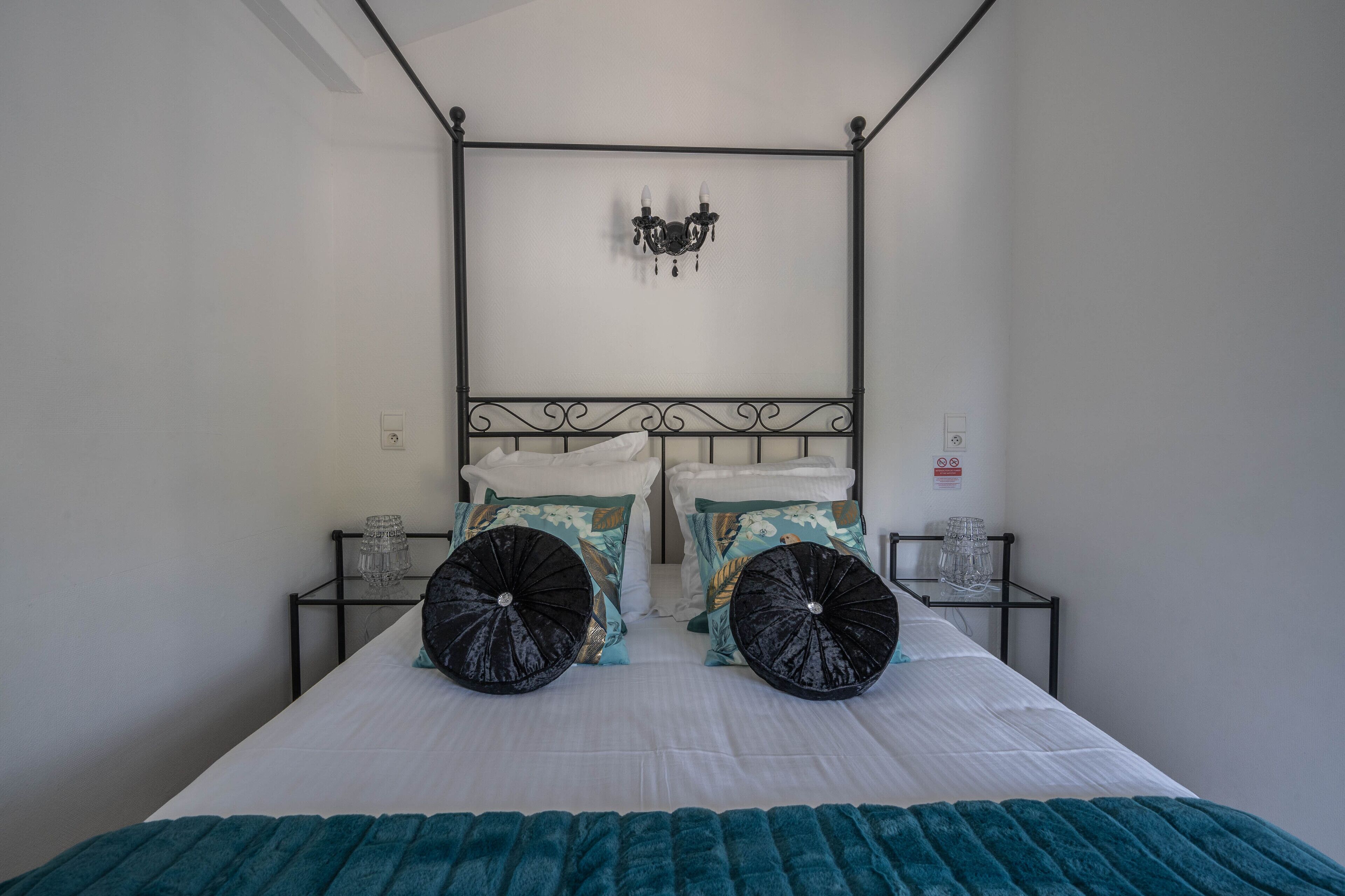 Une chambre à coucher avec un lit à baldaquin, deux tables de chevet et un luminaire fixé au mur.