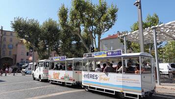 A tram with passengers, parked on a cobblestone street, surrounded by trees and buildings.