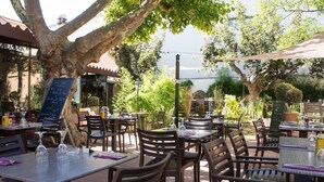Een openluchtrestaurant met tafels en stoelen, omgeven door bomen en begroeiing.